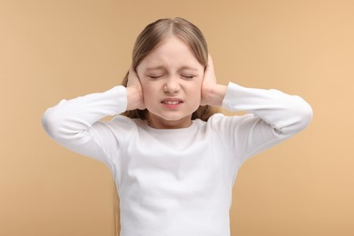 Hearing problem. Little girl suffering from ear pain on pale brown background