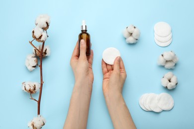 Photo of Woman holding makeup removal product and cotton pad on light blue background, top view