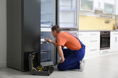 Photo of Male technician with screwdriver repairing refrigerator in kitchen