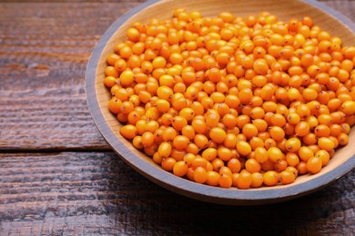 Bowl with fresh ripe sea buckthorn berries on wooden table, closeup