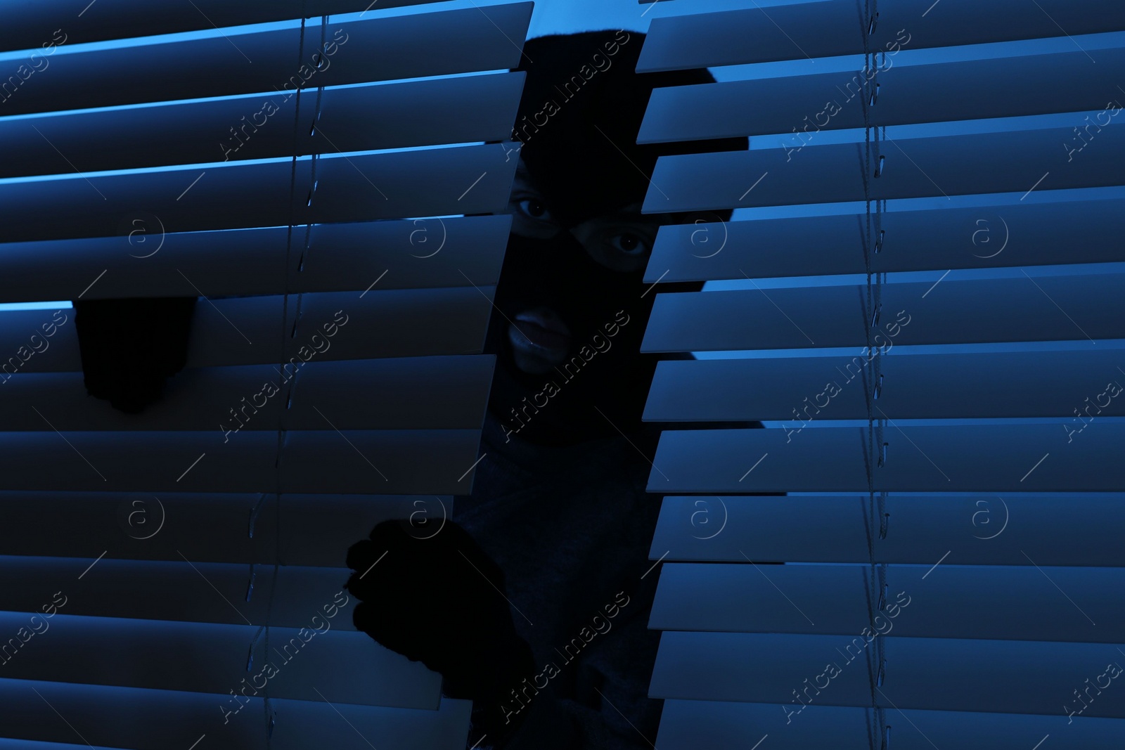 Photo of Thief looking out of blinds at night. Burglary