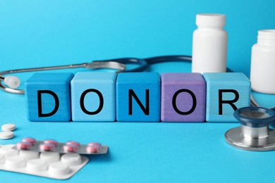 Photo of Word Donor made of wooden cubes, pills and stethoscope on light blue background