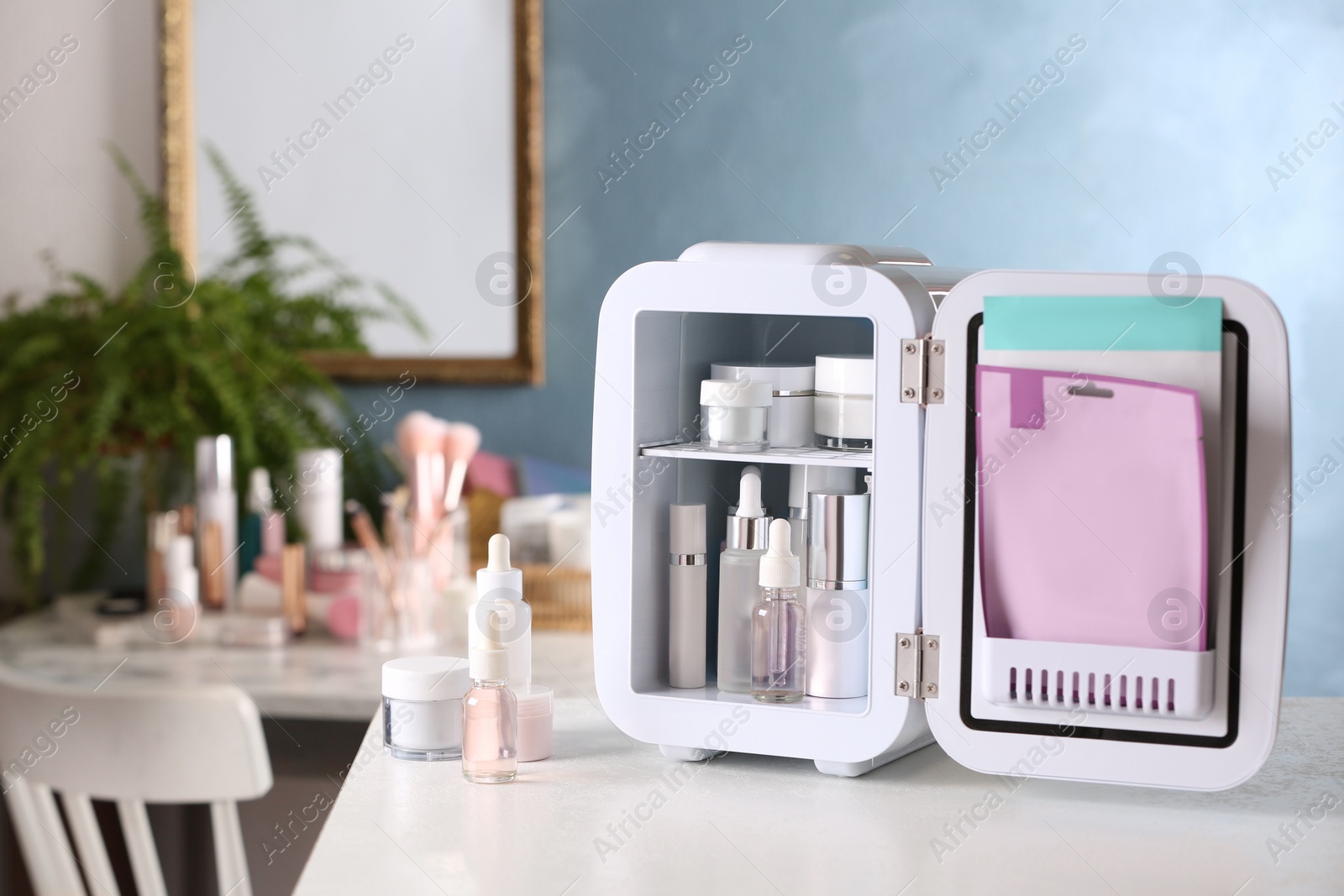 Photo of Open mini cosmetics refrigerator and skin care products on white table