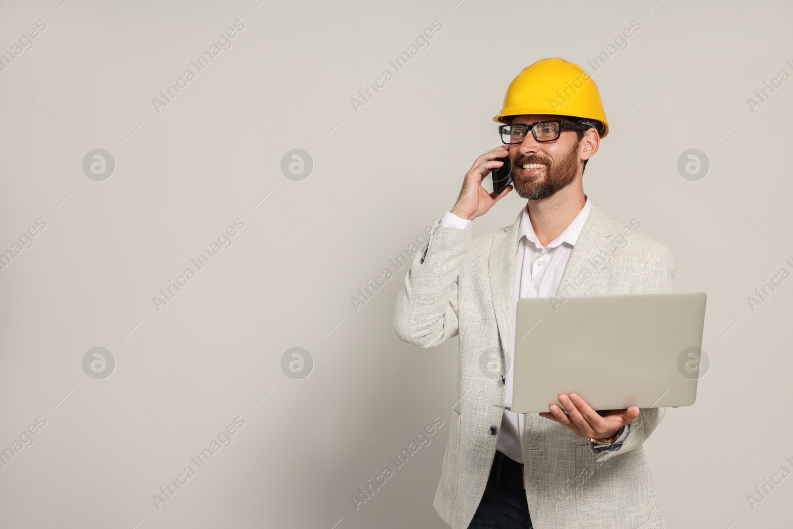 Photo of Professional engineer in hard hat with laptop talking on phone against white background, space for text