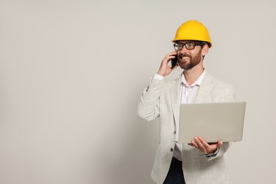 Photo of Professional engineer in hard hat with laptop talking on phone against white background, space for text