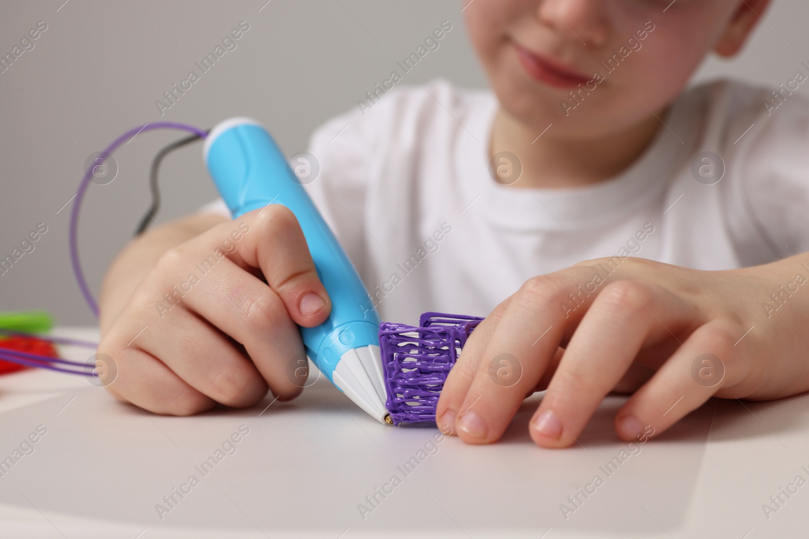 Photo of Boy drawing with stylish 3D pen at white table, closeup