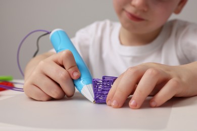 Boy drawing with stylish 3D pen at white table, closeup
