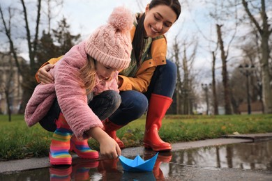 Photo of Little girl and her mother playing with paper boat near puddle in park