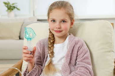Little girl holding nebulizer for inhalation in armchair at home