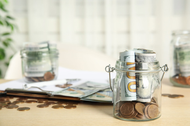 Photo of Glass jar with money on wooden table. Space for text
