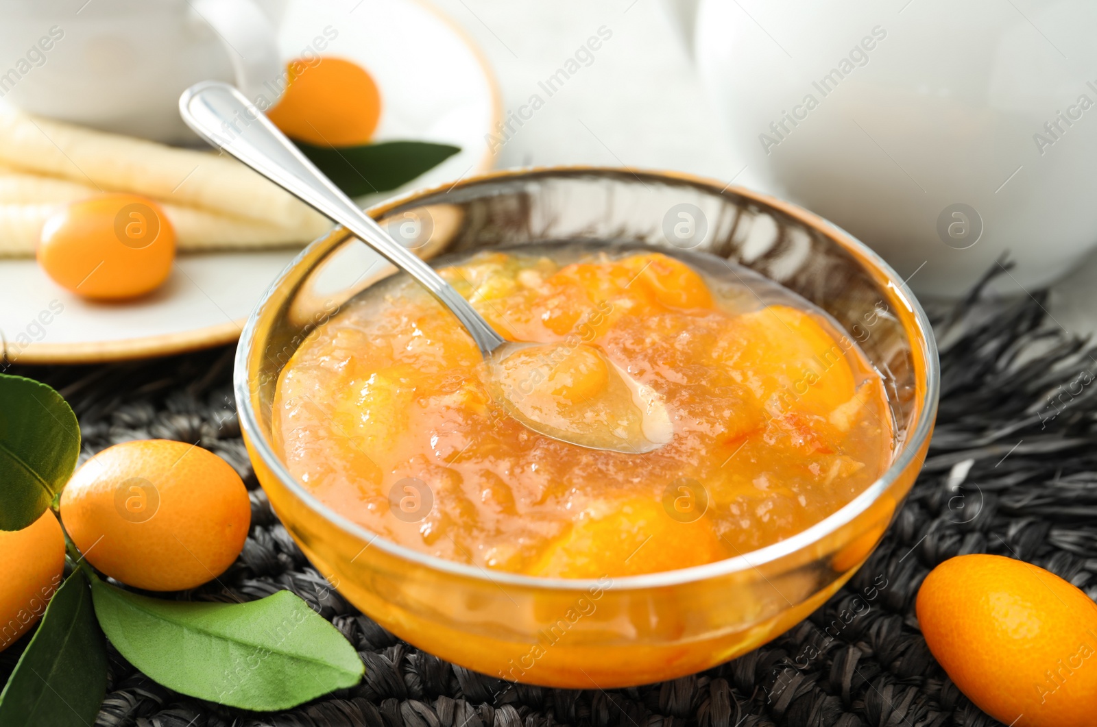 Photo of Delicious kumquat jam and fresh fruits on wicker mat, closeup