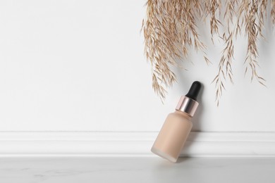 Skin foundation and decorative plant near white wall, space for text. Makeup product
