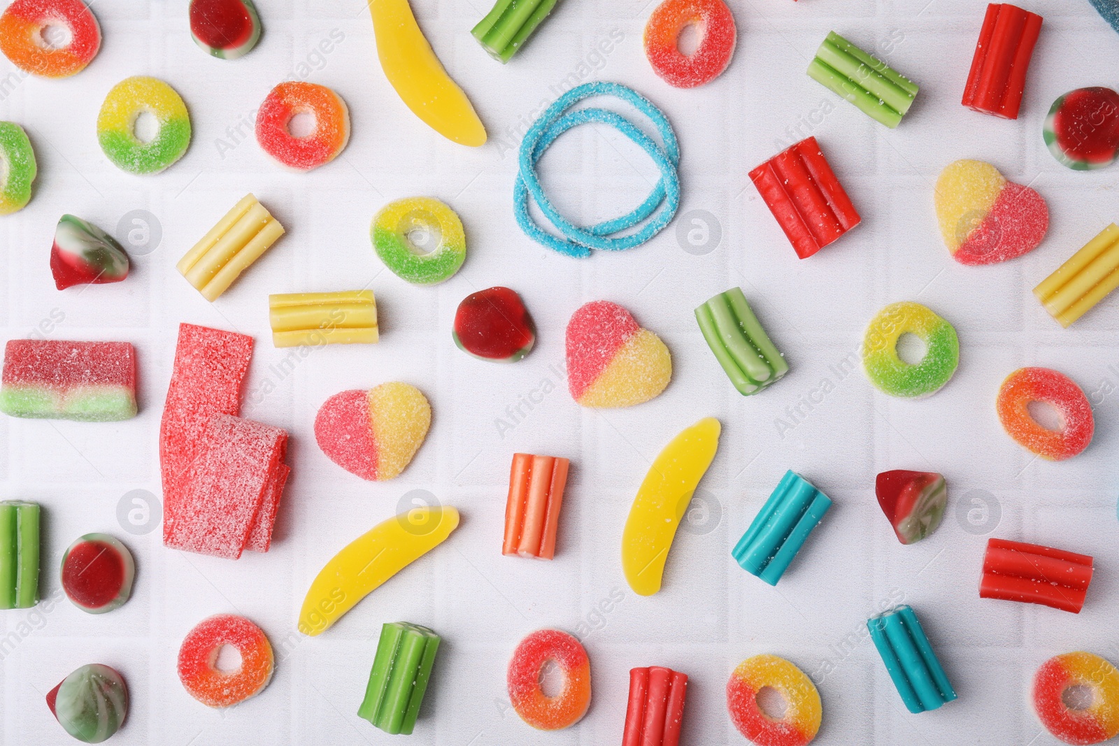 Photo of Many tasty colorful jelly candies on white tiled table, flat lay