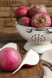 Photo of Cut and whole red turnips on wooden board, closeup