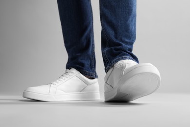 Photo of Man wearing stylish white sneakers on grey background, closeup