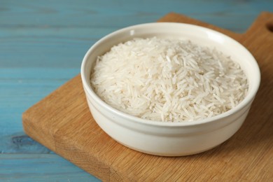 Photo of Raw basmati rice in bowl on light blue wooden table, closeup