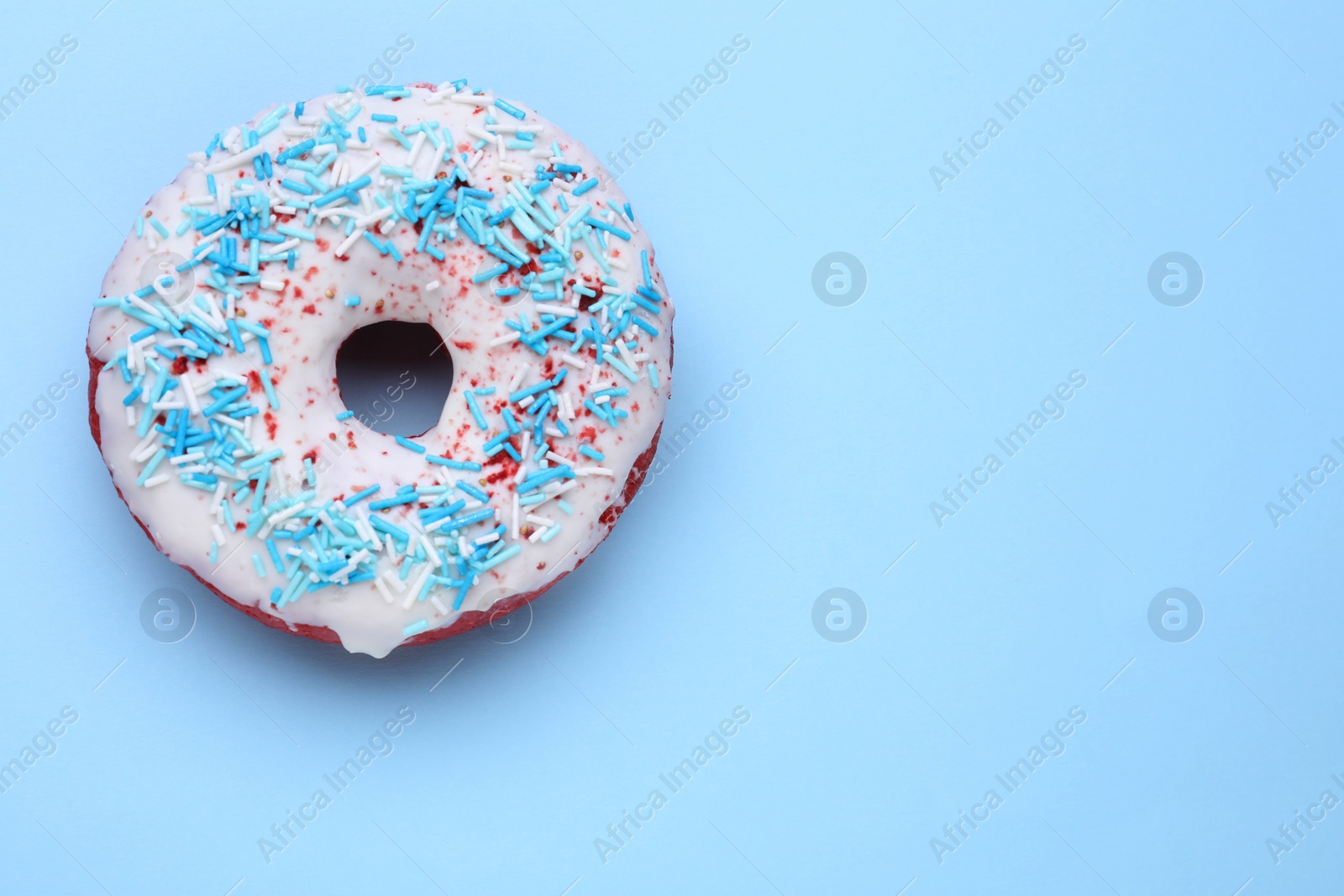 Photo of Glazed donut decorated with sprinkles on light blue background, top view. Space for text. Tasty confectionery