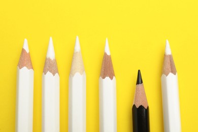 Photo of Flat lay composition with black and white pencils on yellow background. Racism concept