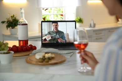 Photo of Friends drinking wine while communicating through online video conference in kitchen. Social distancing during coronavirus pandemic