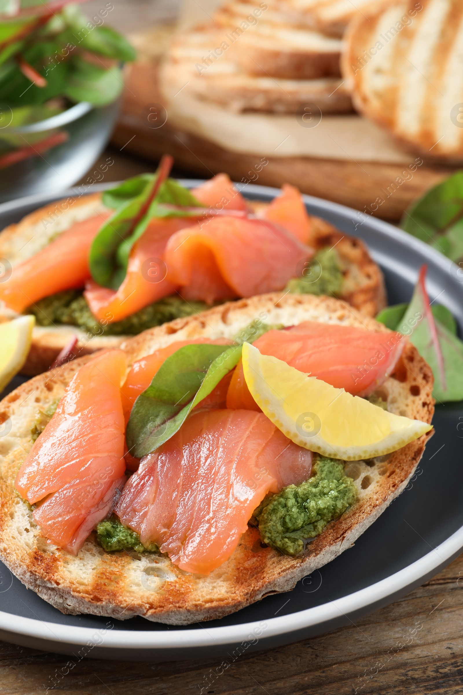 Photo of Delicious bruschettas with salmon and pesto sauce on wooden table, closeup