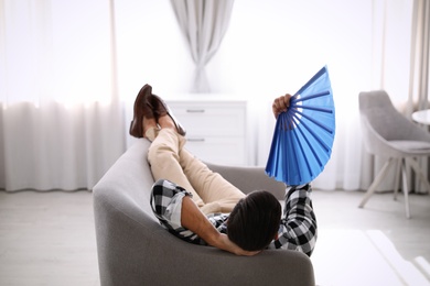 Photo of Man with hand fan lying on sofa. Summer season