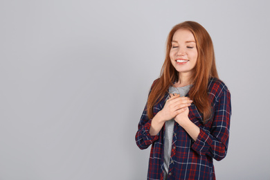 Photo of Beautiful grateful woman with hands on chest against light grey background. Space for text