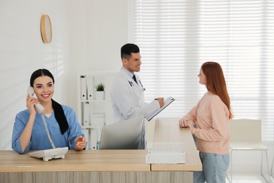 Photo of Receptionist talking on phone while doctor working with patient in hospital
