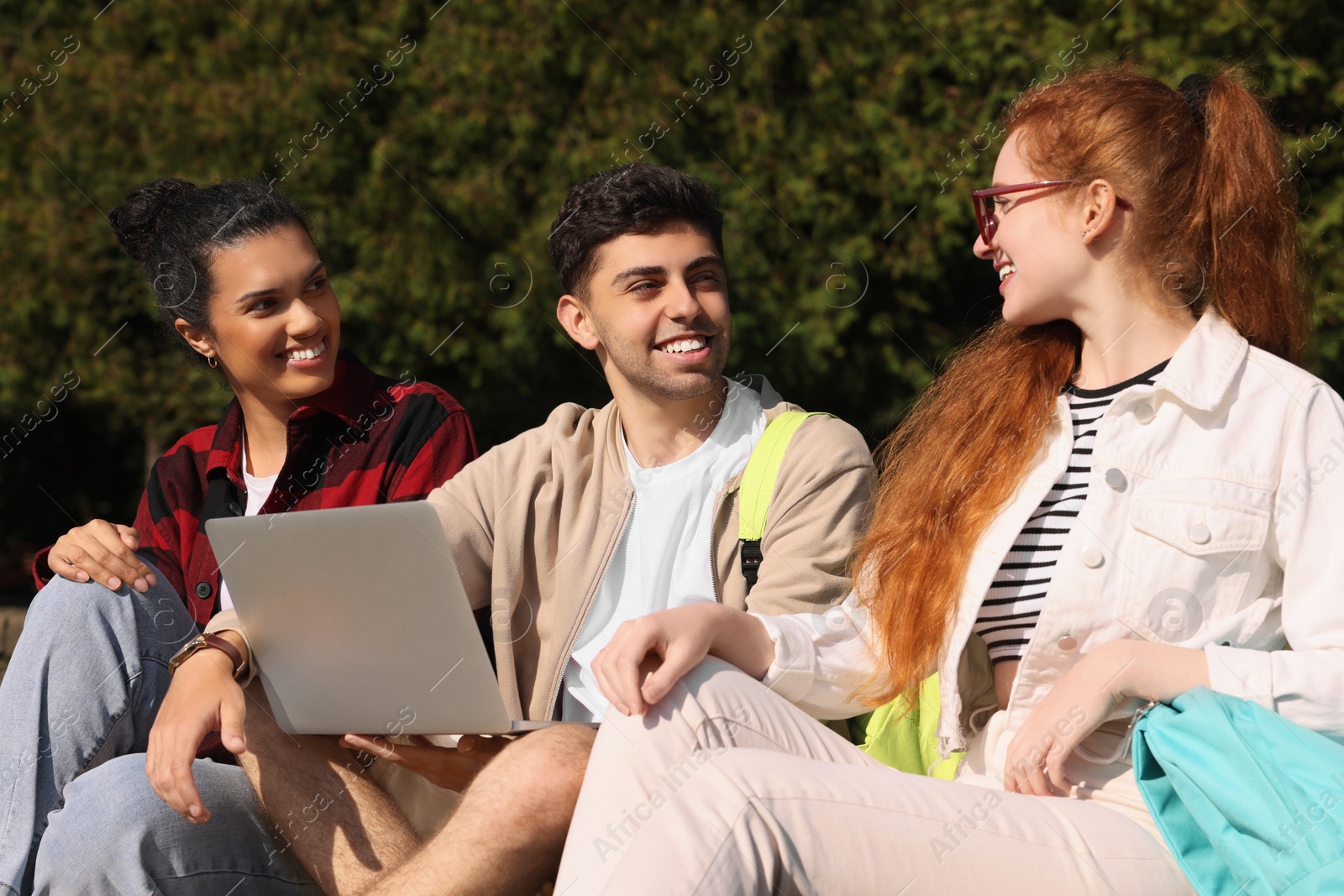 Photo of Happy young students studying with laptop together in park