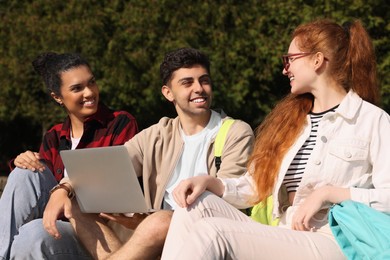 Photo of Happy young students studying with laptop together in park