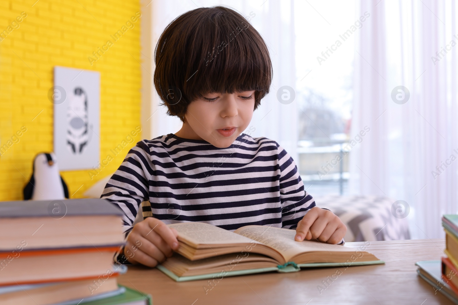 Photo of Cute little boy reading book at table in room