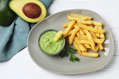 Photo of Plate with french fries, guacamole dip, parsley and avocado served on white wooden table, top view