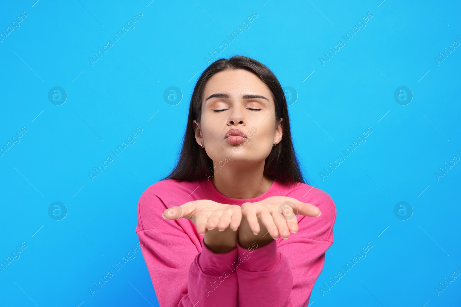 Photo of Beautiful young woman blowing kiss on light blue background