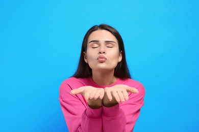 Beautiful young woman blowing kiss on light blue background