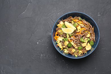 Photo of Stir-fry. Delicious cooked noodles with chicken and vegetables in bowl on gray textured table, top view. Space for text