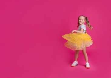 Photo of Cute little girl in tutu skirt dancing on pink background. space for text
