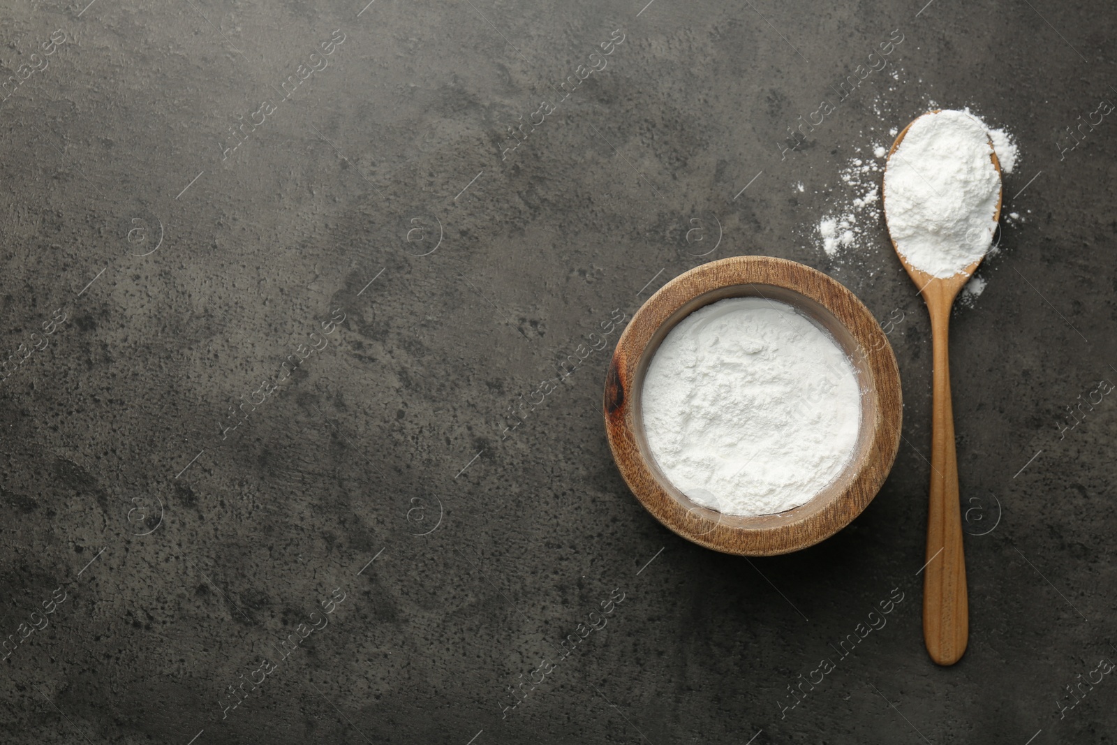 Photo of Baking powder in bowl and spoon on grey textured table, top view. Space for text