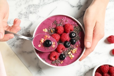 Woman eating tasty acai smoothie with raspberries and chia seeds at white marble table, top view