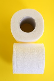 Photo of Soft toilet paper rolls on yellow background, top view