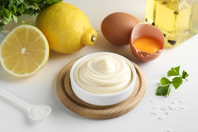 Photo of Fresh mayonnaise sauce in bowl and ingredients on white wooden table