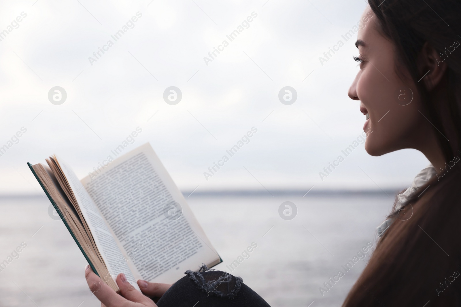 Photo of Woman reading book near river on cloudy day