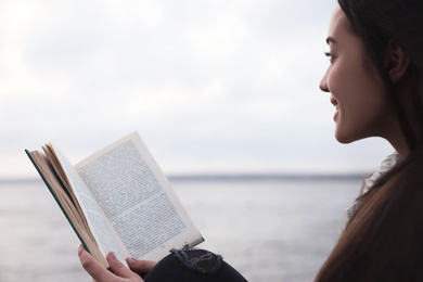 Photo of Woman reading book near river on cloudy day