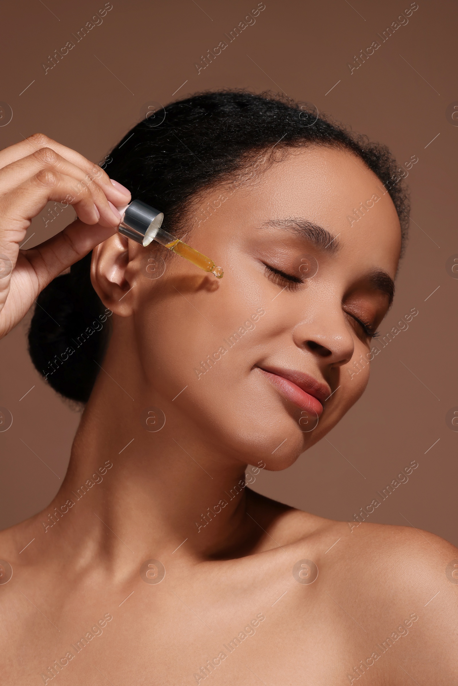 Photo of Beautiful woman applying serum onto her face on brown background