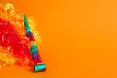 Photo of Clown wig and party blower on orange background, space for text