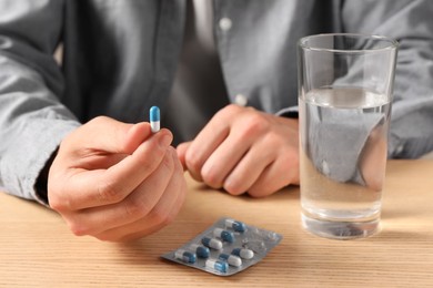 Photo of Man holding pill near glass of water at wooden table, closeup