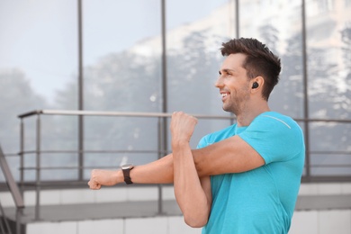 Photo of Young sportsman with wireless earphones stretching on city street