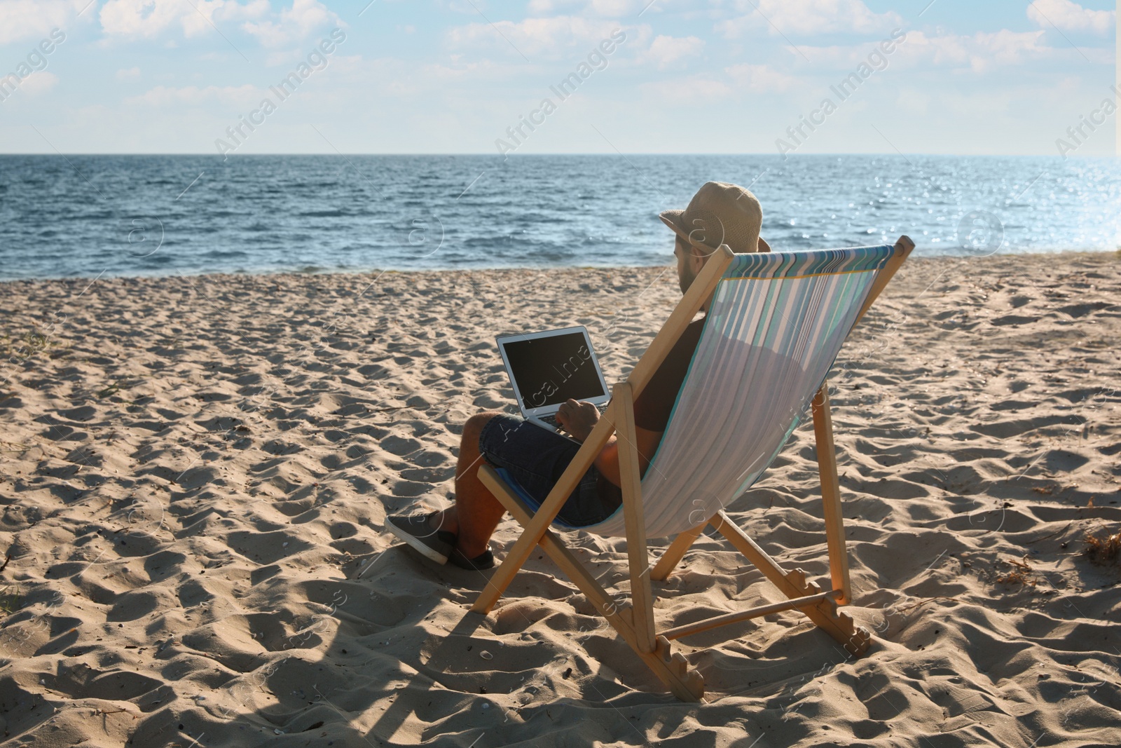 Photo of Man working with laptop in deck chair on beach. Space for text