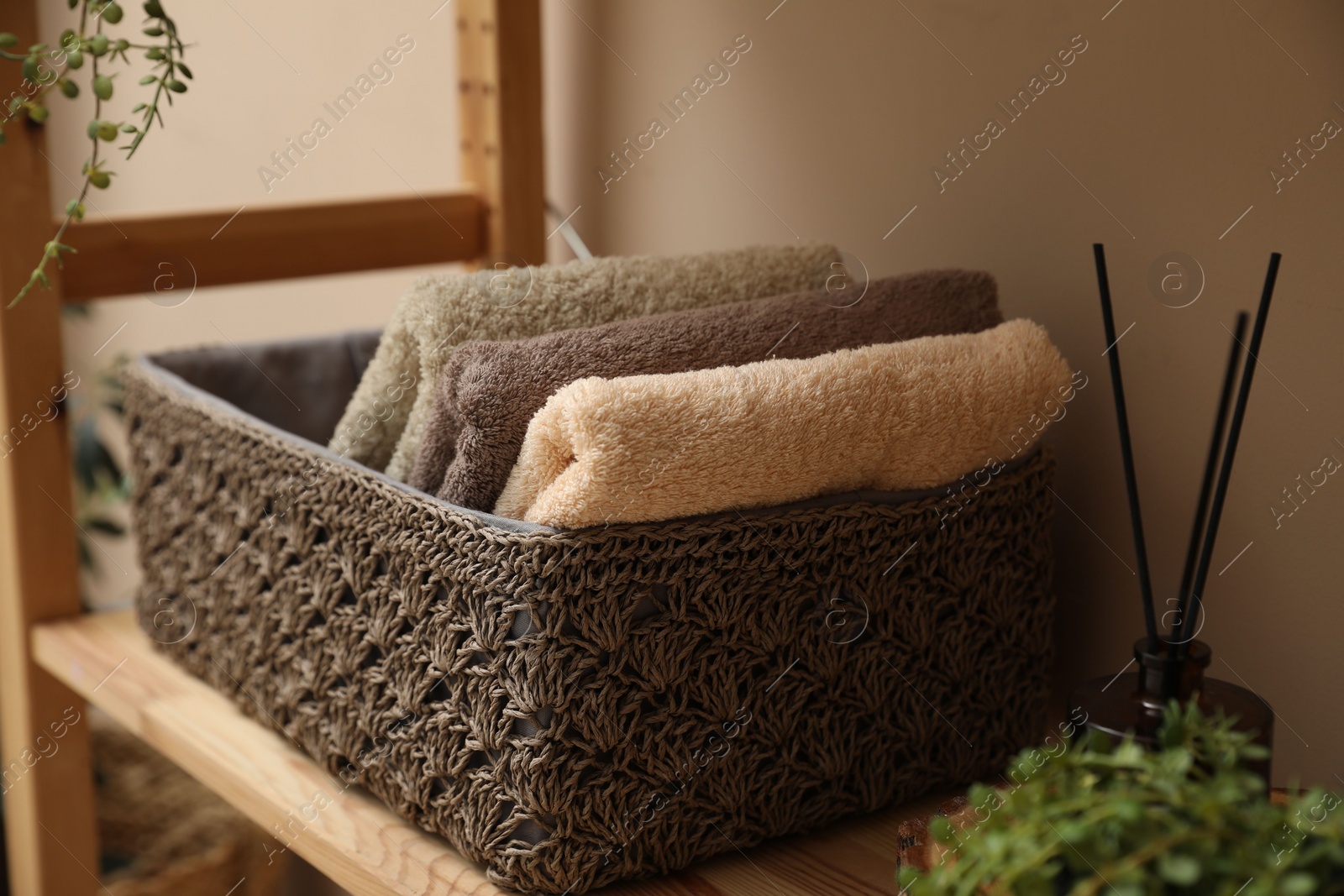 Photo of Soft towels in storage box and air freshener on shelf indoors, closeup