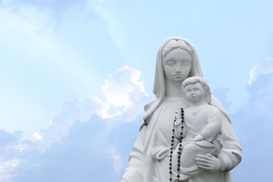 Photo of Beautiful statue of Virgin Mary and baby Jesus with rosary beads outdoors. Space for text