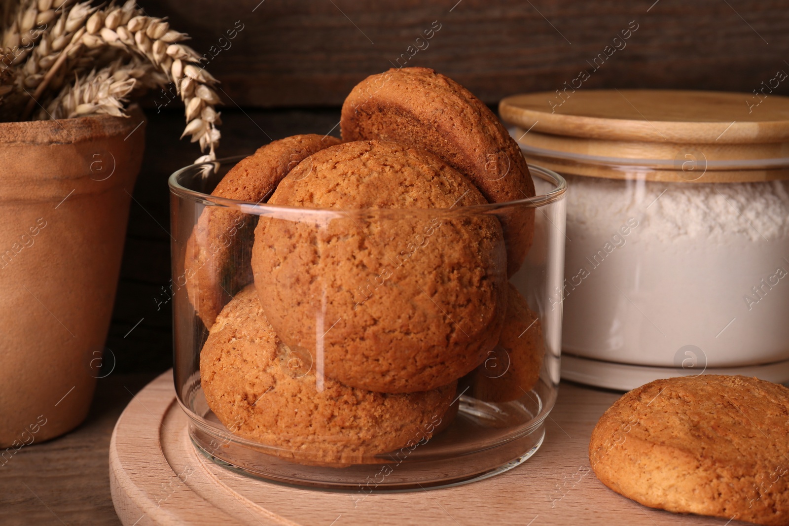 Photo of Cookies and jar of wheat flour on wooden board, closeup view