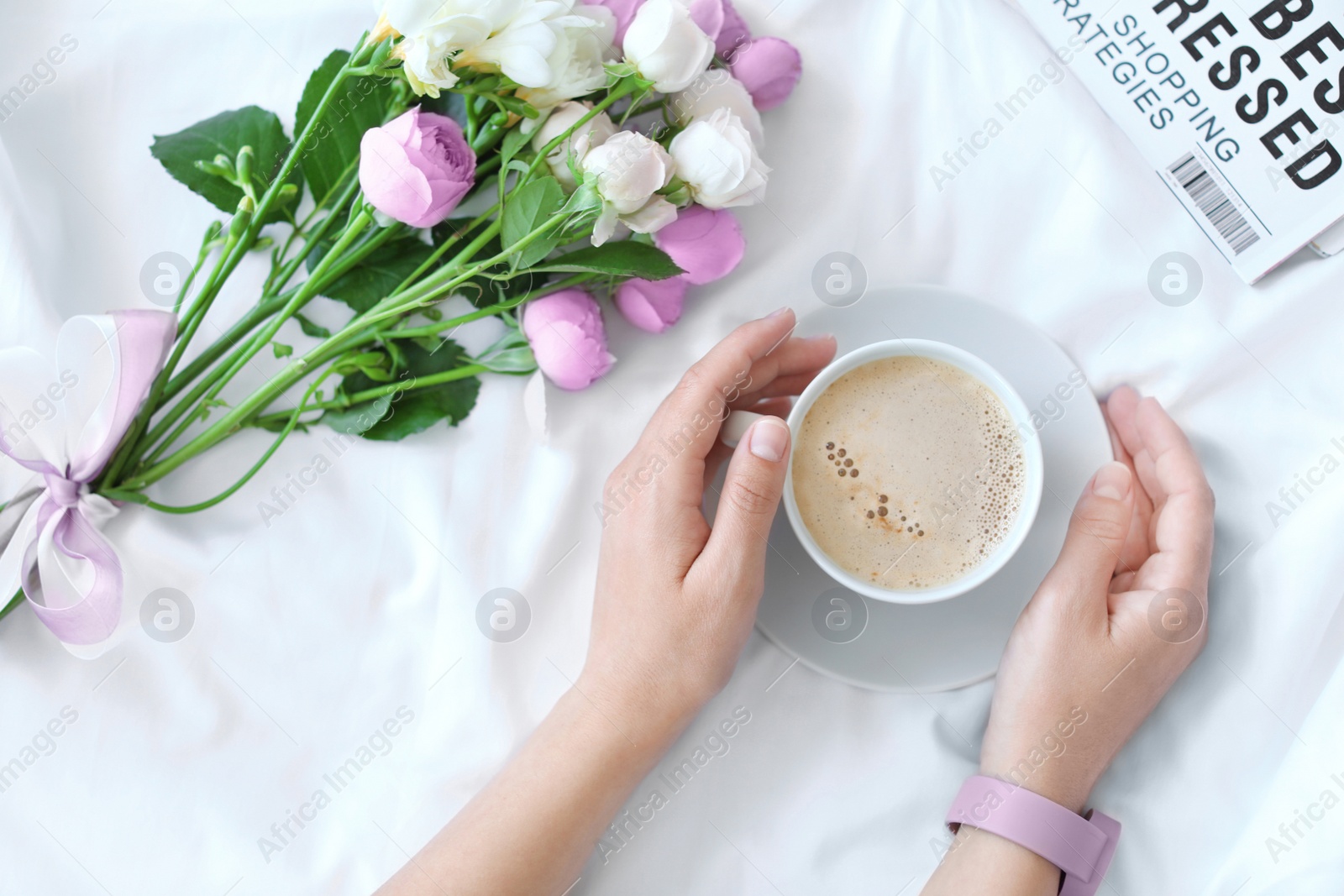 Photo of Woman with cup of coffee, beautiful flowers and magazine on fabric, top view